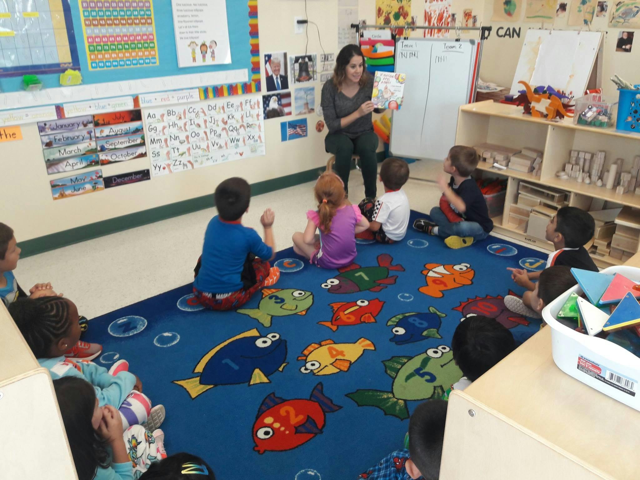 Person reading a book to children sitting on a fish-patterned rug