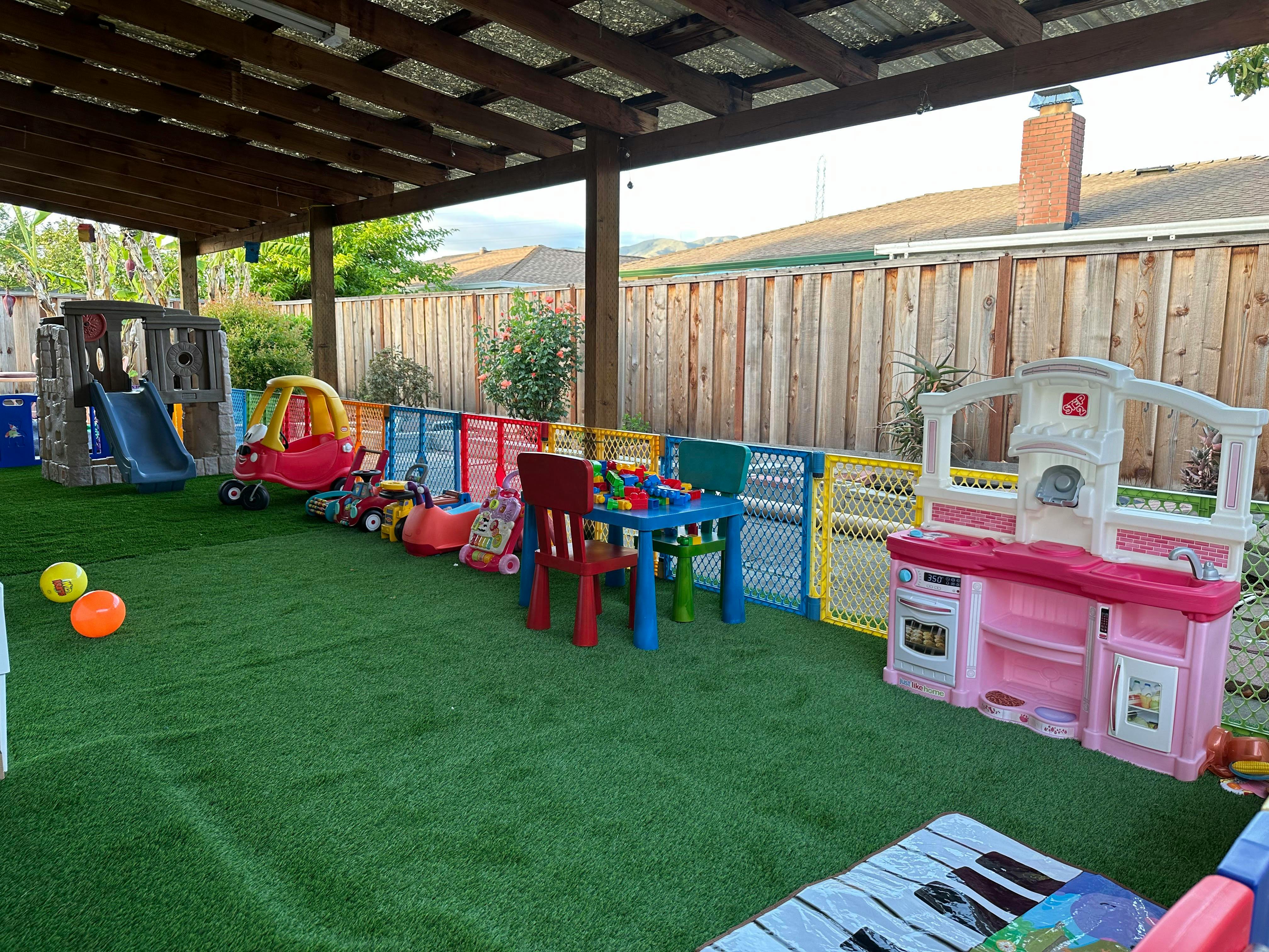 Playground area with slide, ride-on toys, and toy kitchen under a covered patio