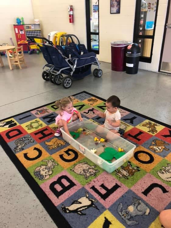 Two children playing with toys in a container of water on an alphabet rug