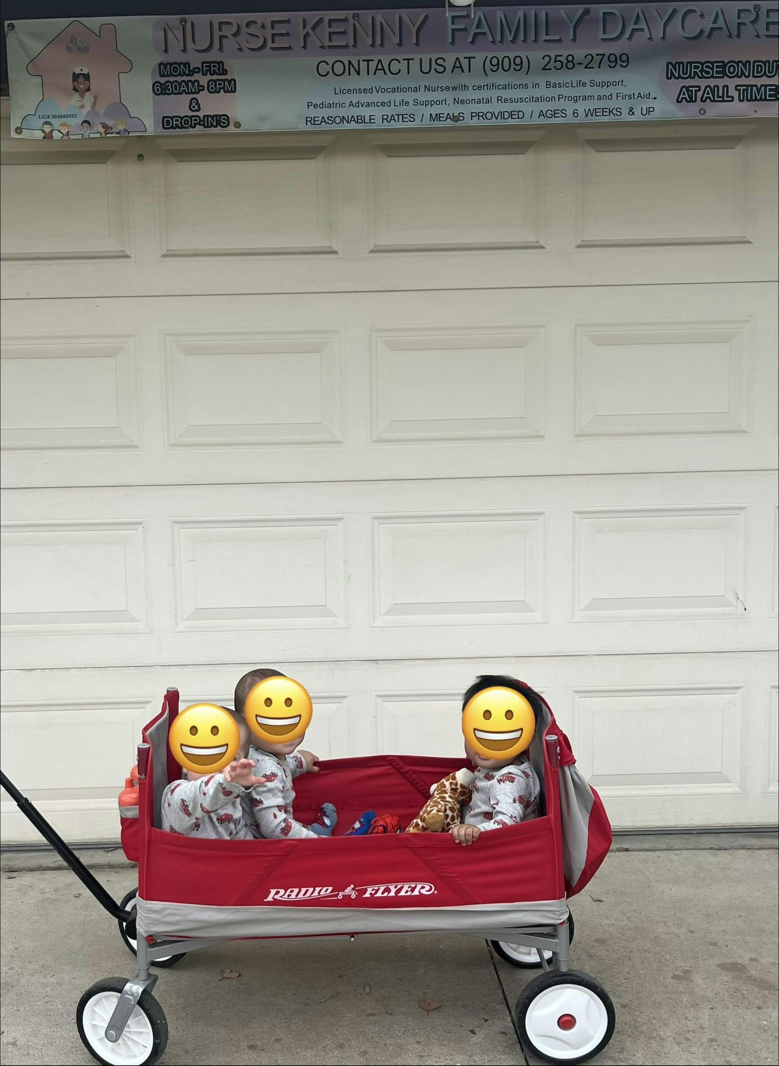 Three children sitting in a red wagon in front of a daycare sign