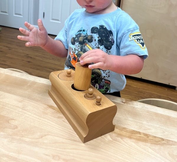 Child placing a wooden cylinder into a cylinder block toy at a table