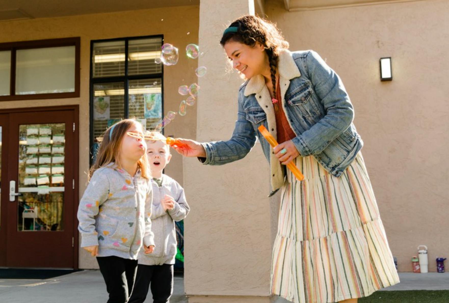 Person blowing bubbles with two children watching outdoors
