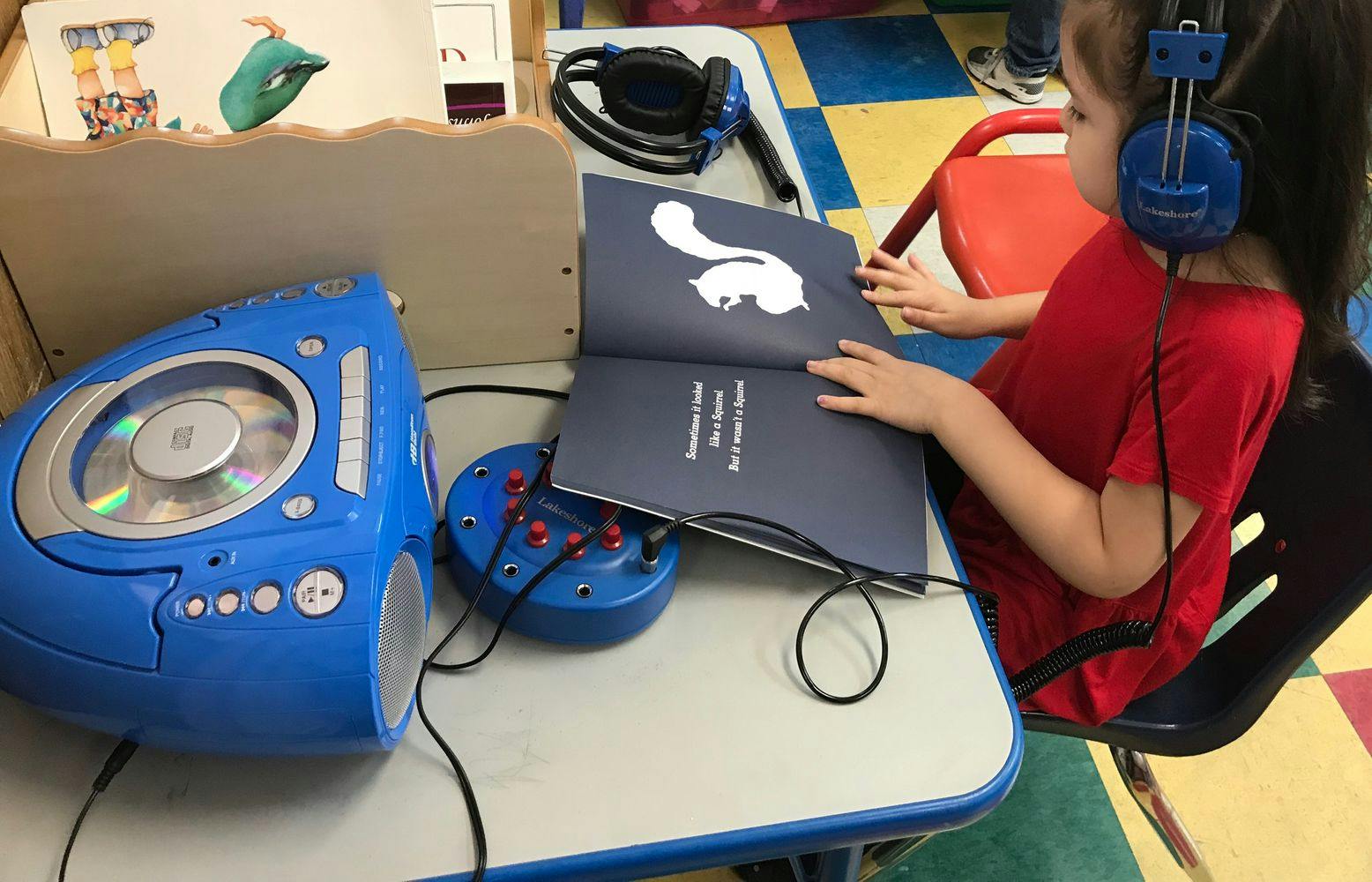 Child wearing headphones and reading a book with a CD player nearby