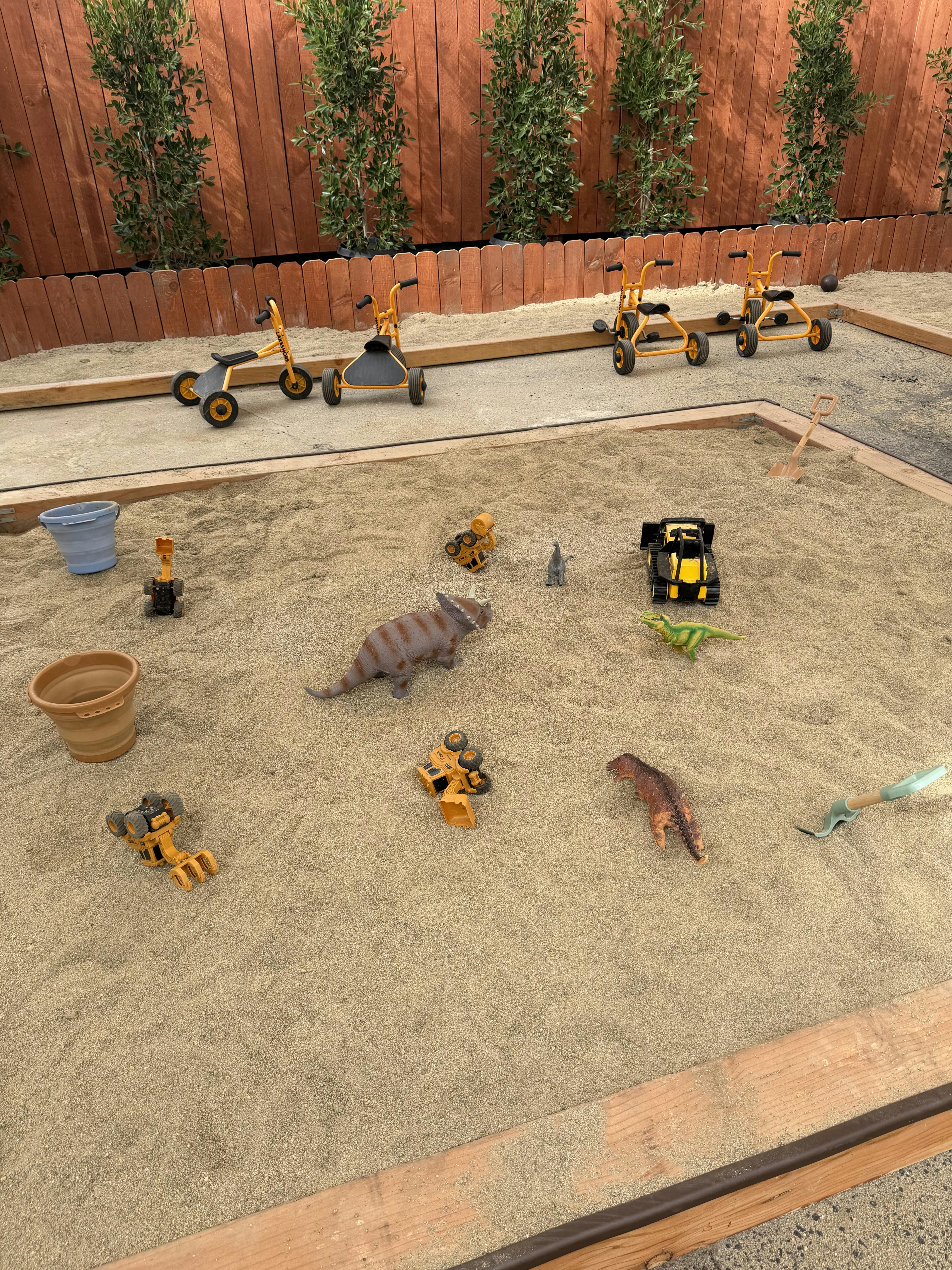 Sandbox with toy dinosaurs, construction vehicles, and a shovel
