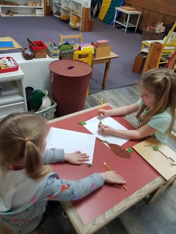 Two children drawing at a table in a classroom