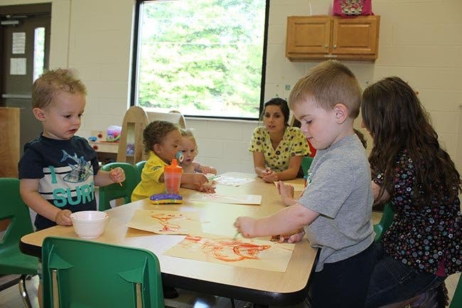 Children and an adult sitting at a table doing an art activity