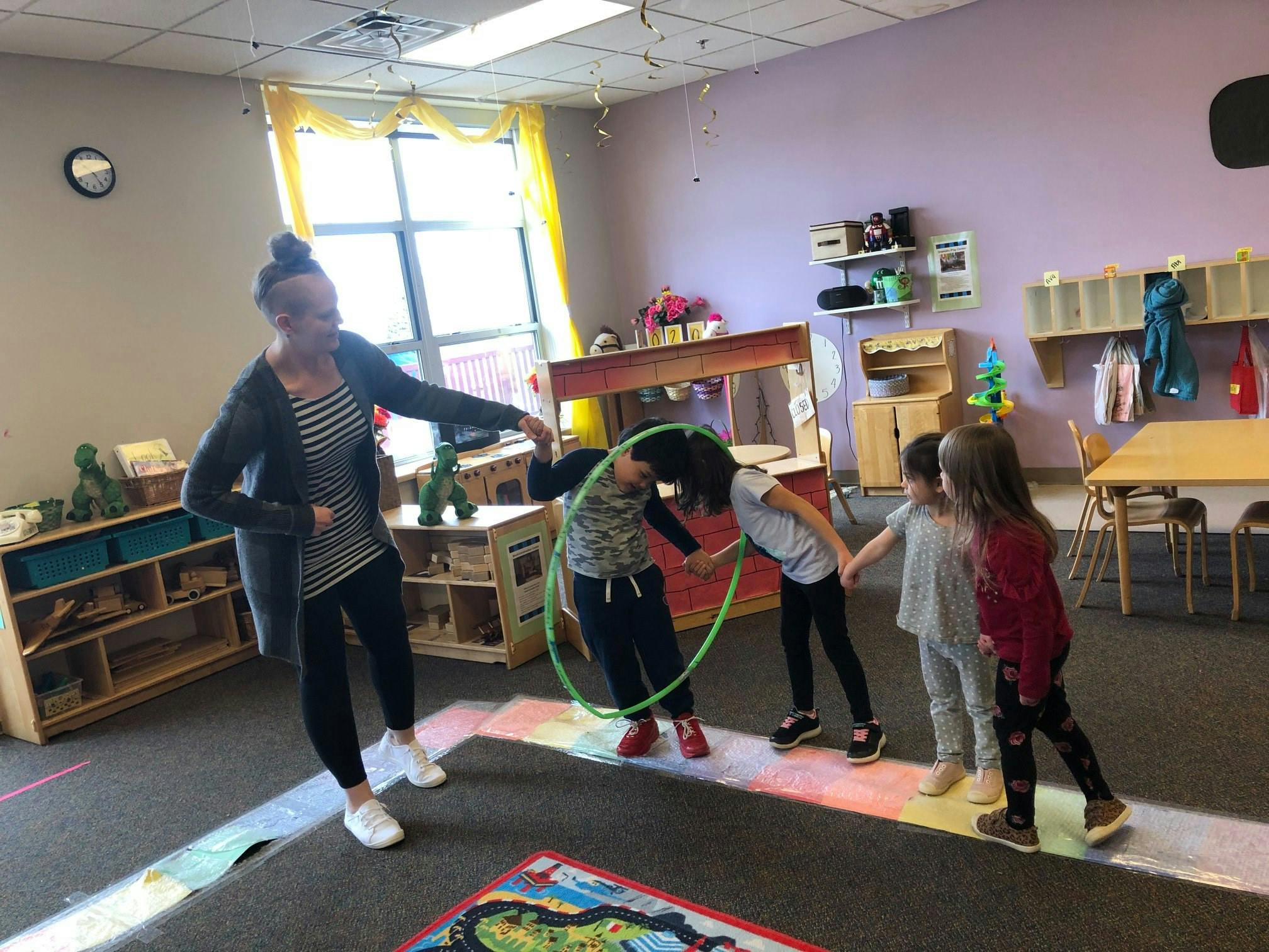 Person and children playing with hula hoops in a classroom