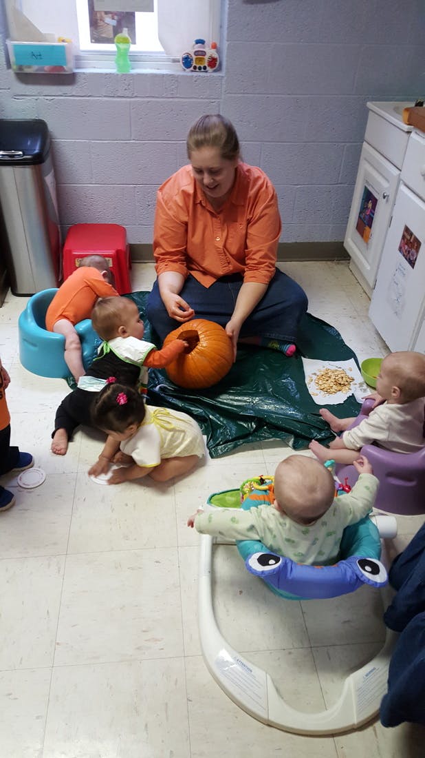 Person sitting on floor with multiple children and a pumpkin