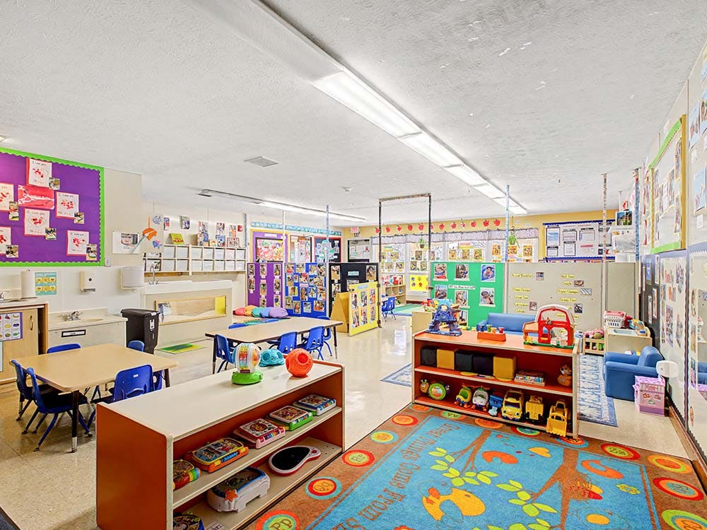 empty preschool classroom with tables, chairs, and play areas