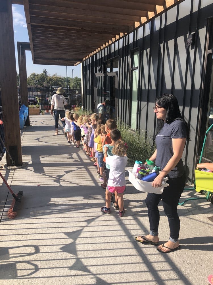 Person holding a bin of water bottles, children in a line behind her
