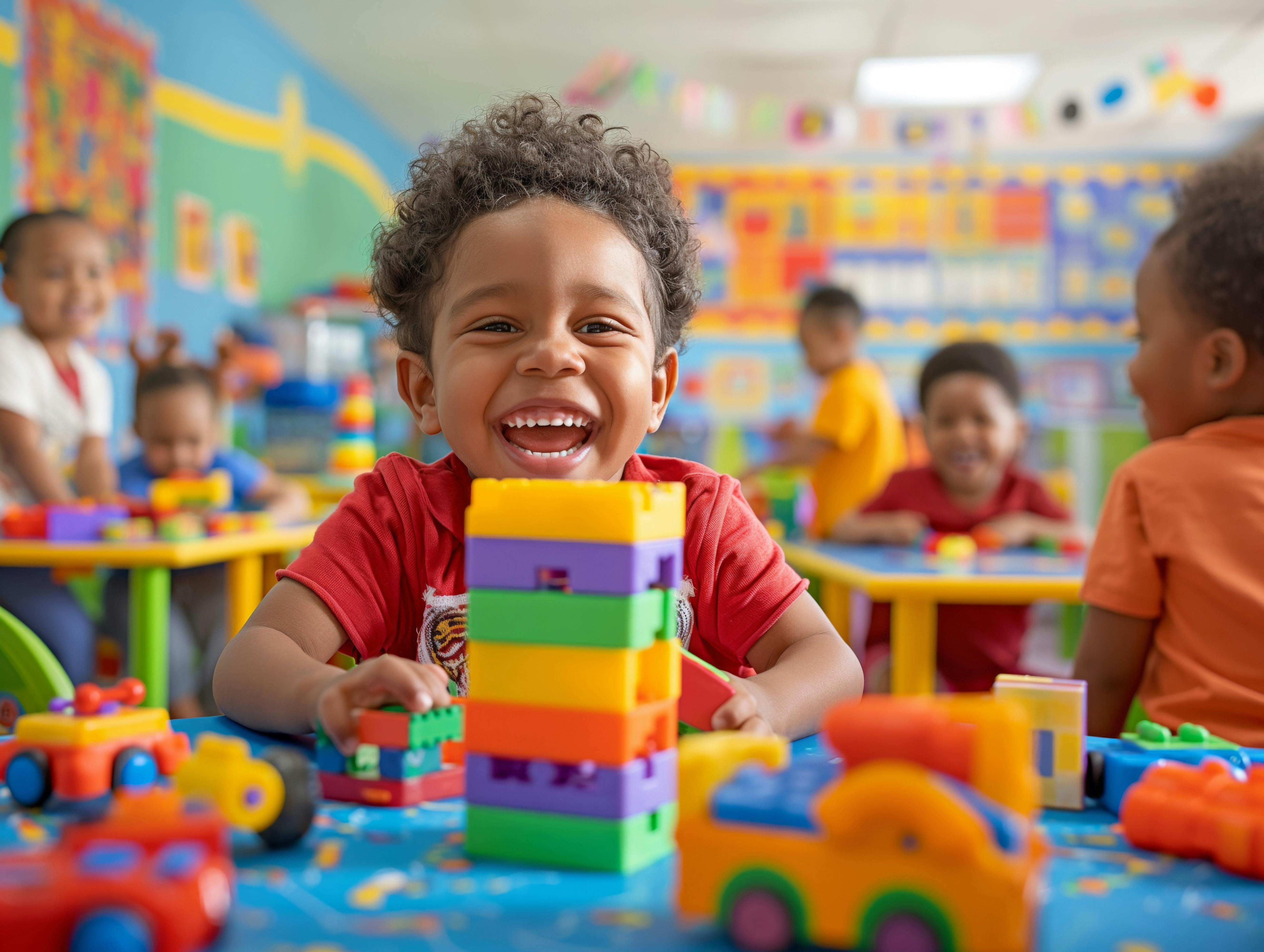 Child smiling with a tower of colorful blocks in a classroom