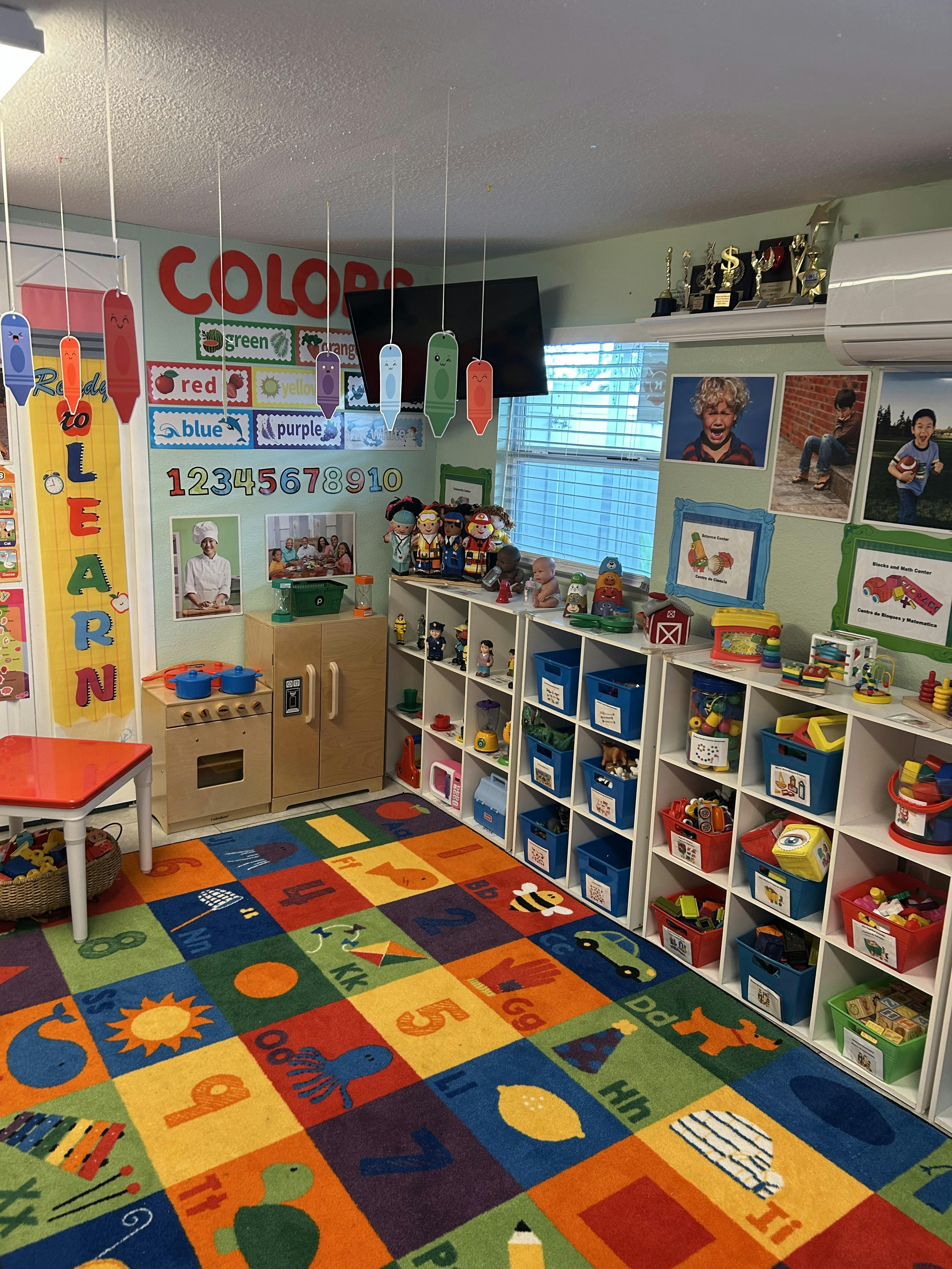 A classroom with a colorful alphabet rug, toy kitchen, and shelves of toys