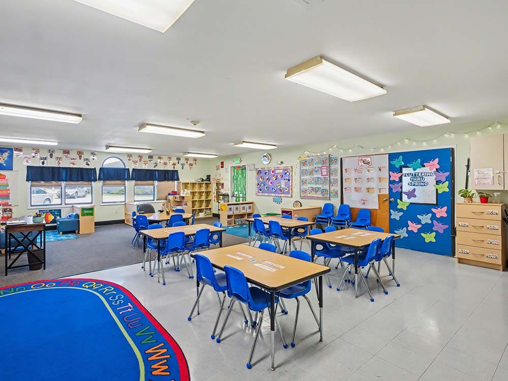 Classroom with small tables and chairs, a blue rug, and decorated walls