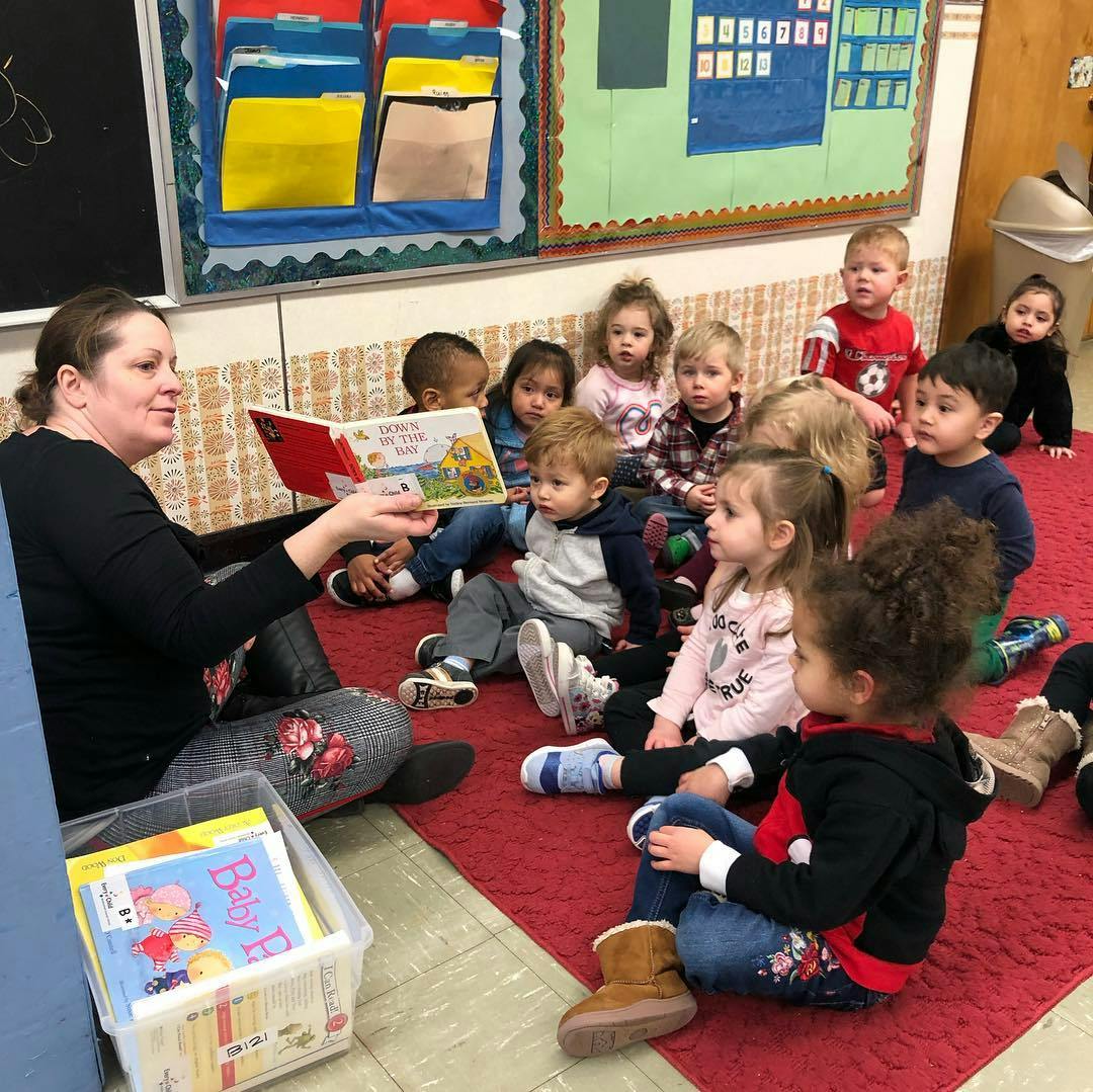 Person reading a book to a group of children in a classroom