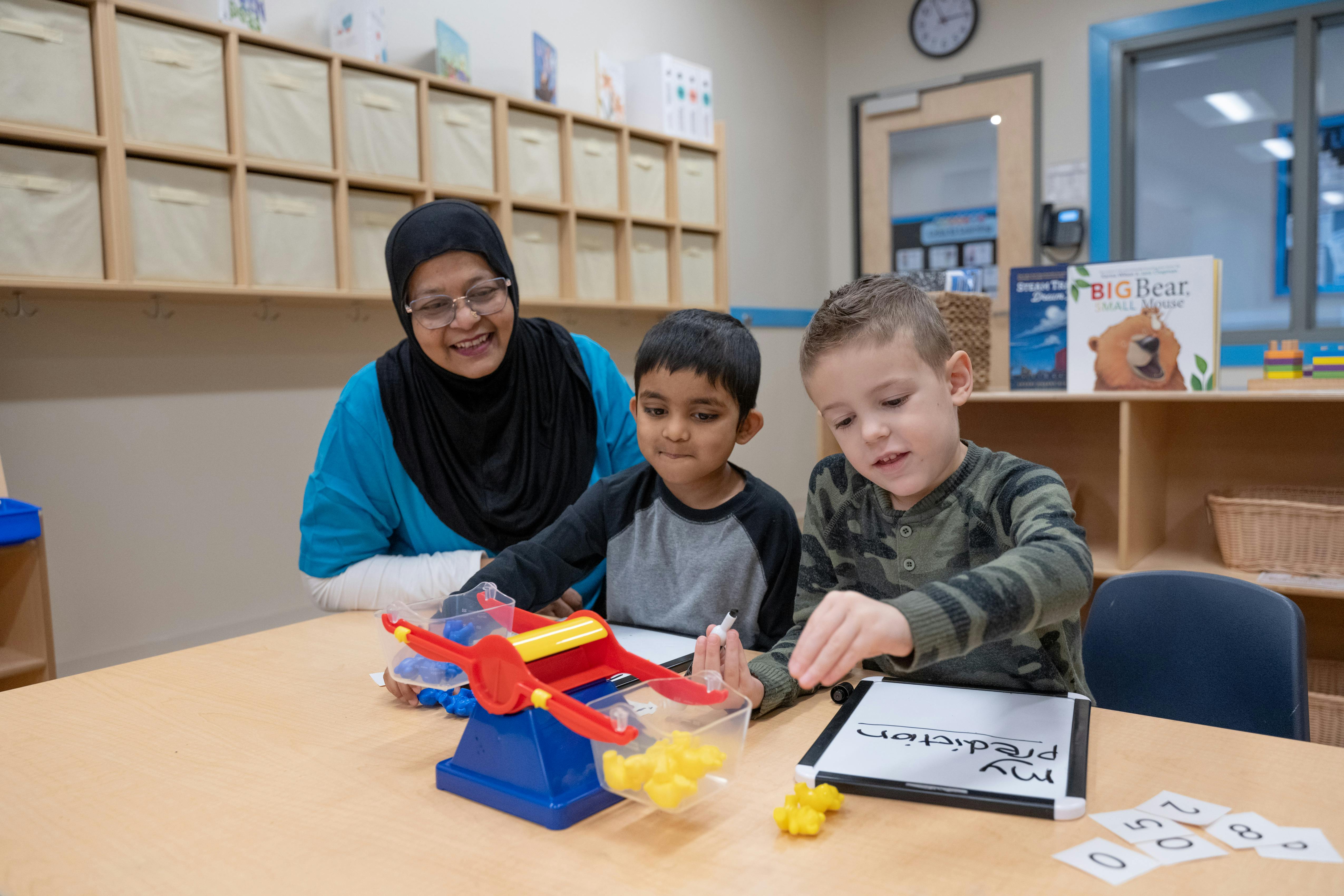 Adult and two children at a table with a toy scale and learning materials
