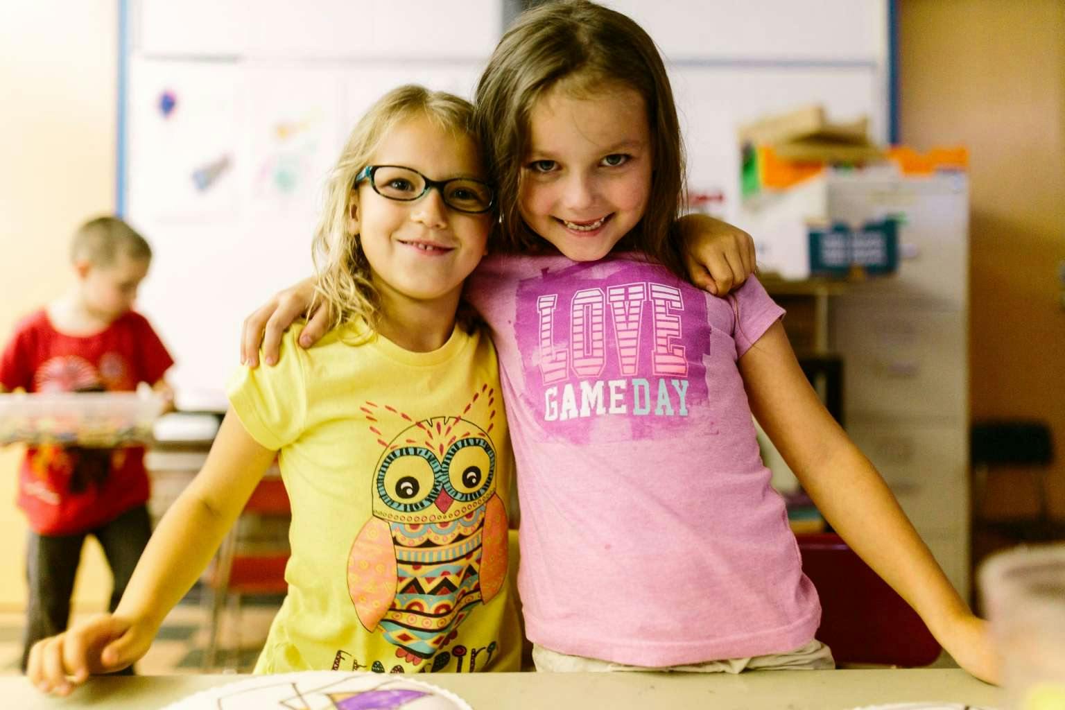 Two children with arms around each other in a classroom