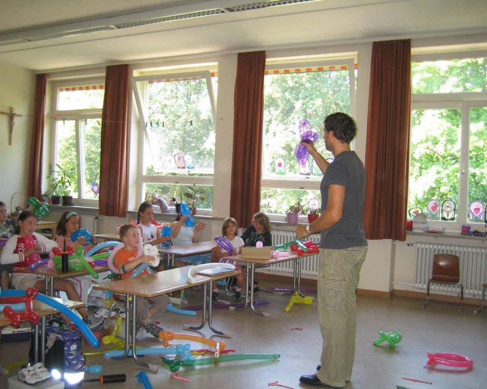 Person making balloon animals for children in a classroom