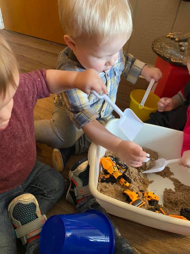 Two children playing with sand and toy trucks in a bin
