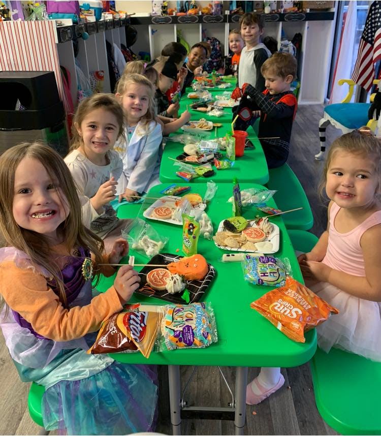 Children sitting at green tables with snacks