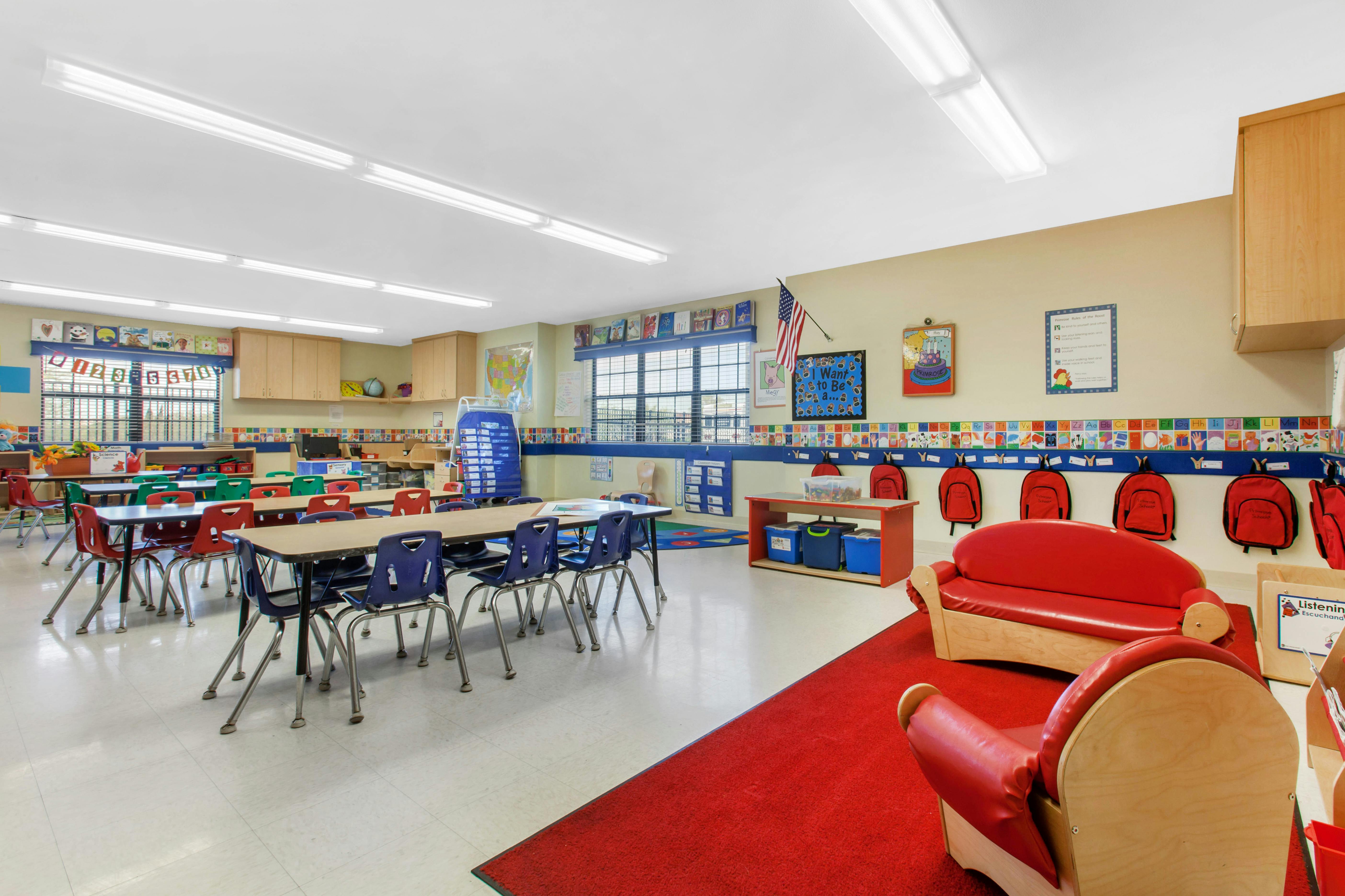 Classroom with child-sized tables and chairs, red couches, and backpacks on hooks