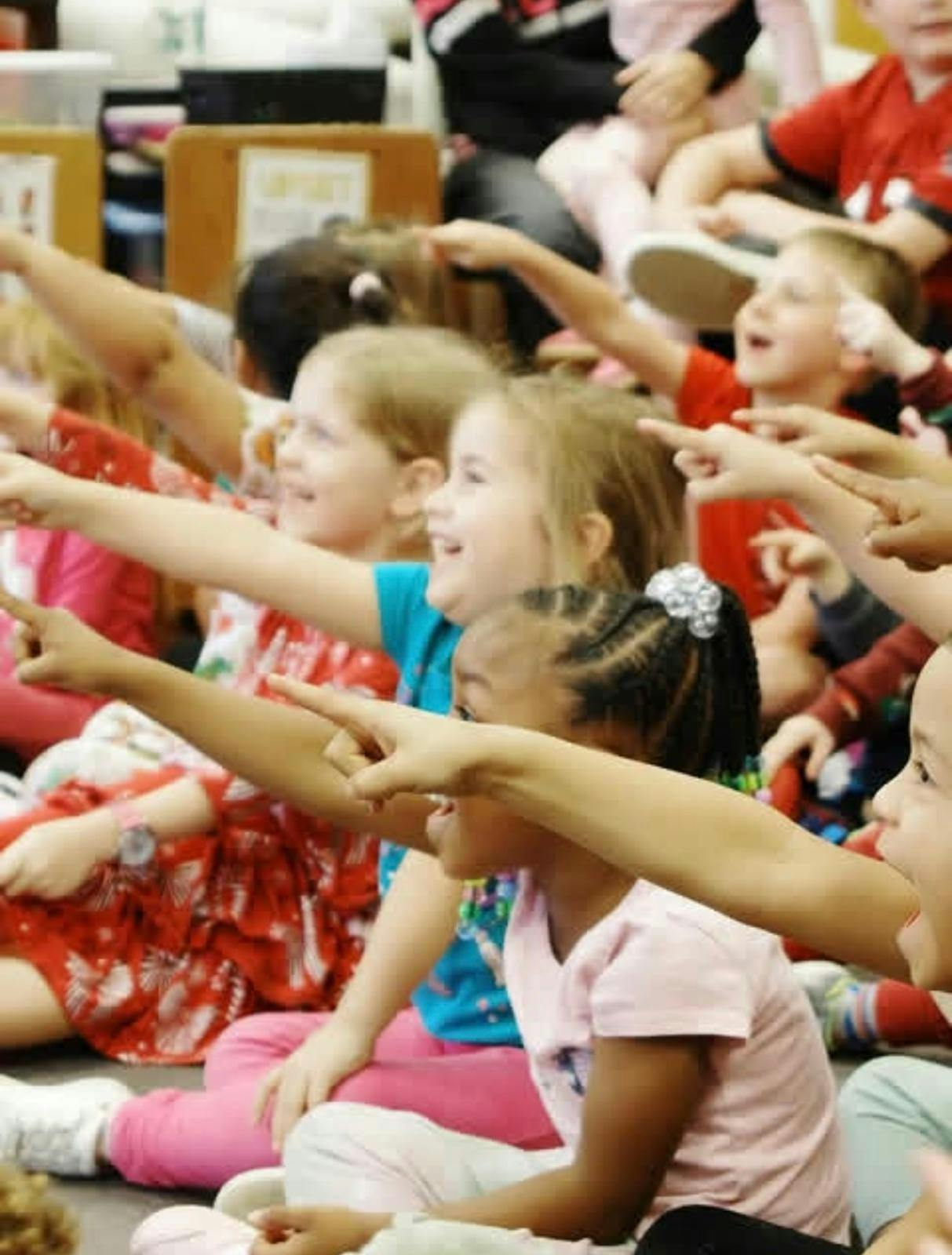 Group of children sitting on the floor and pointing in the same direction