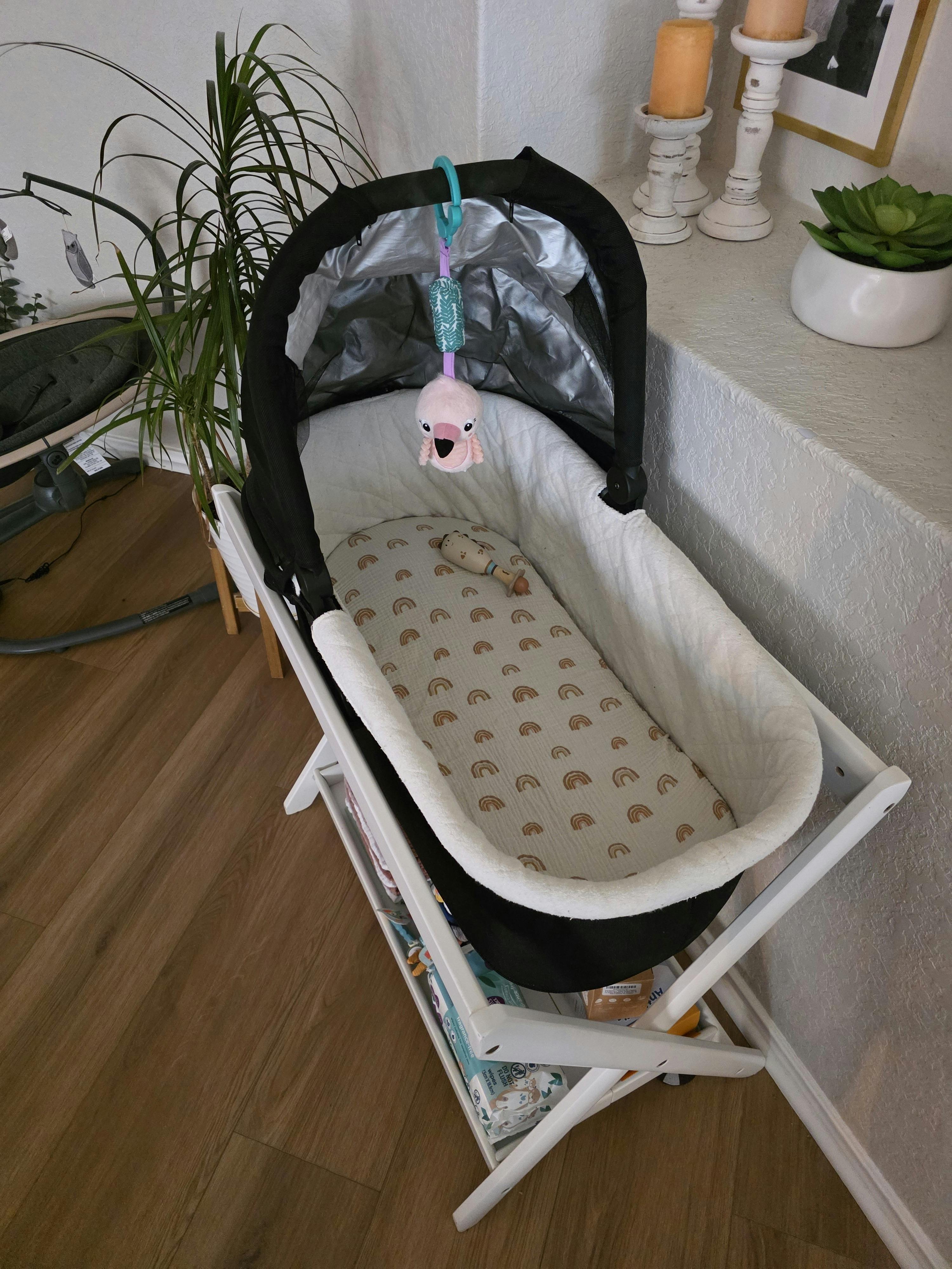 Baby bassinet with a rainbow pattern sheet and hanging plush toy