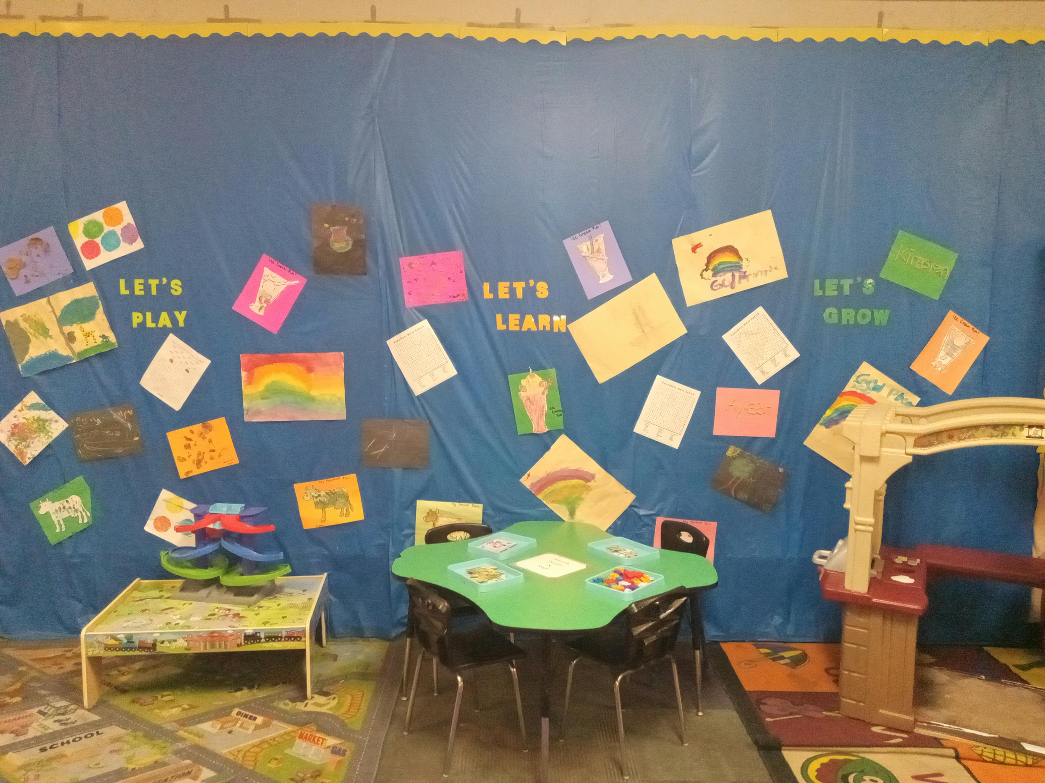 Classroom wall with children's artwork and text "Let's Play" and "Let's Learn"