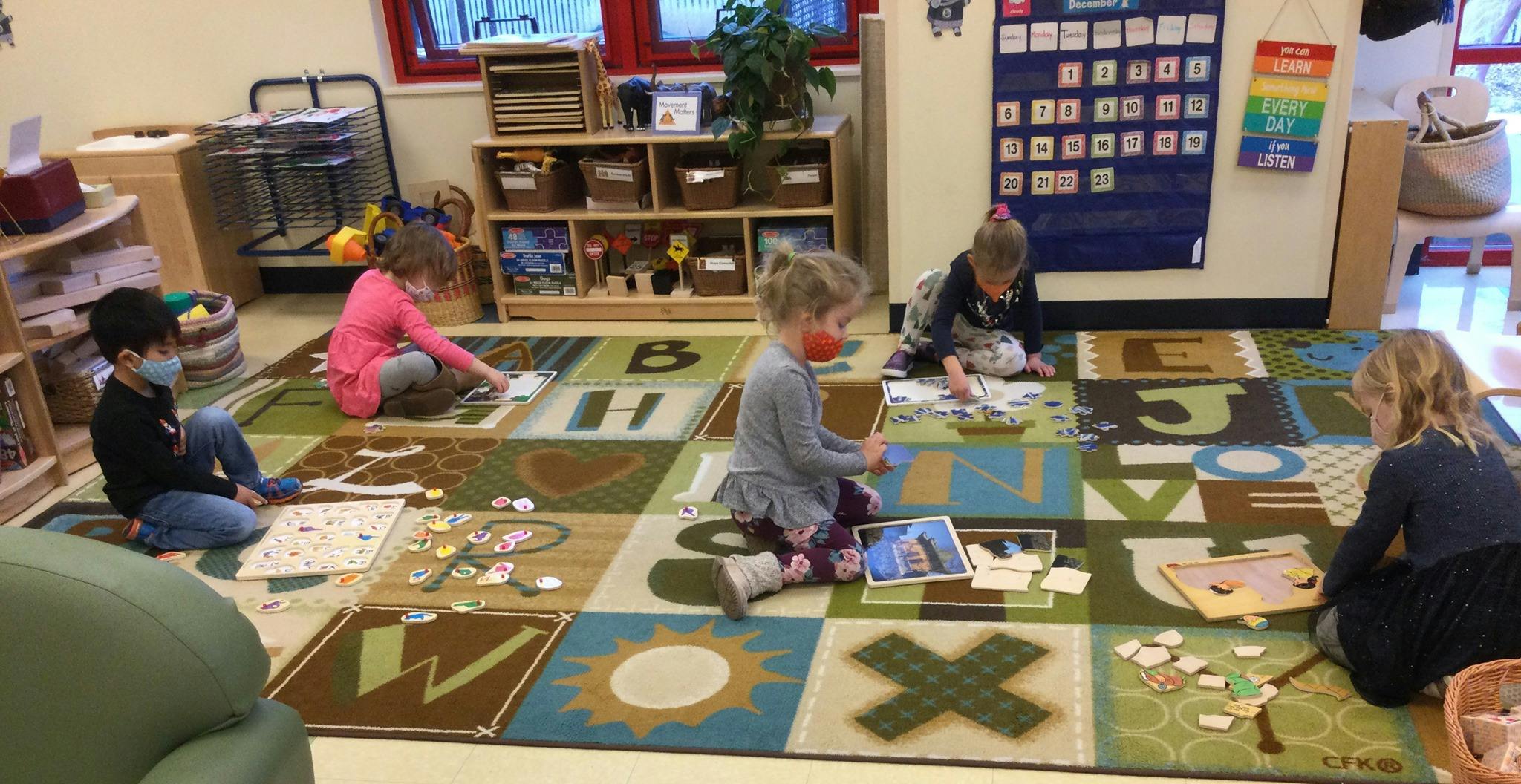 Children playing with learning materials on a rug in a classroom