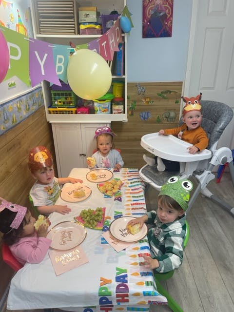 Children in party hats eating cake at a table with a Happy Birthday tablecloth