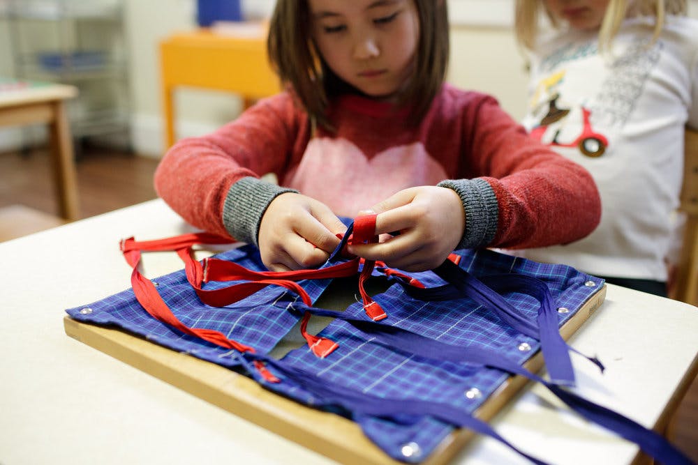 Child tying red and blue ribbons on a fabric board