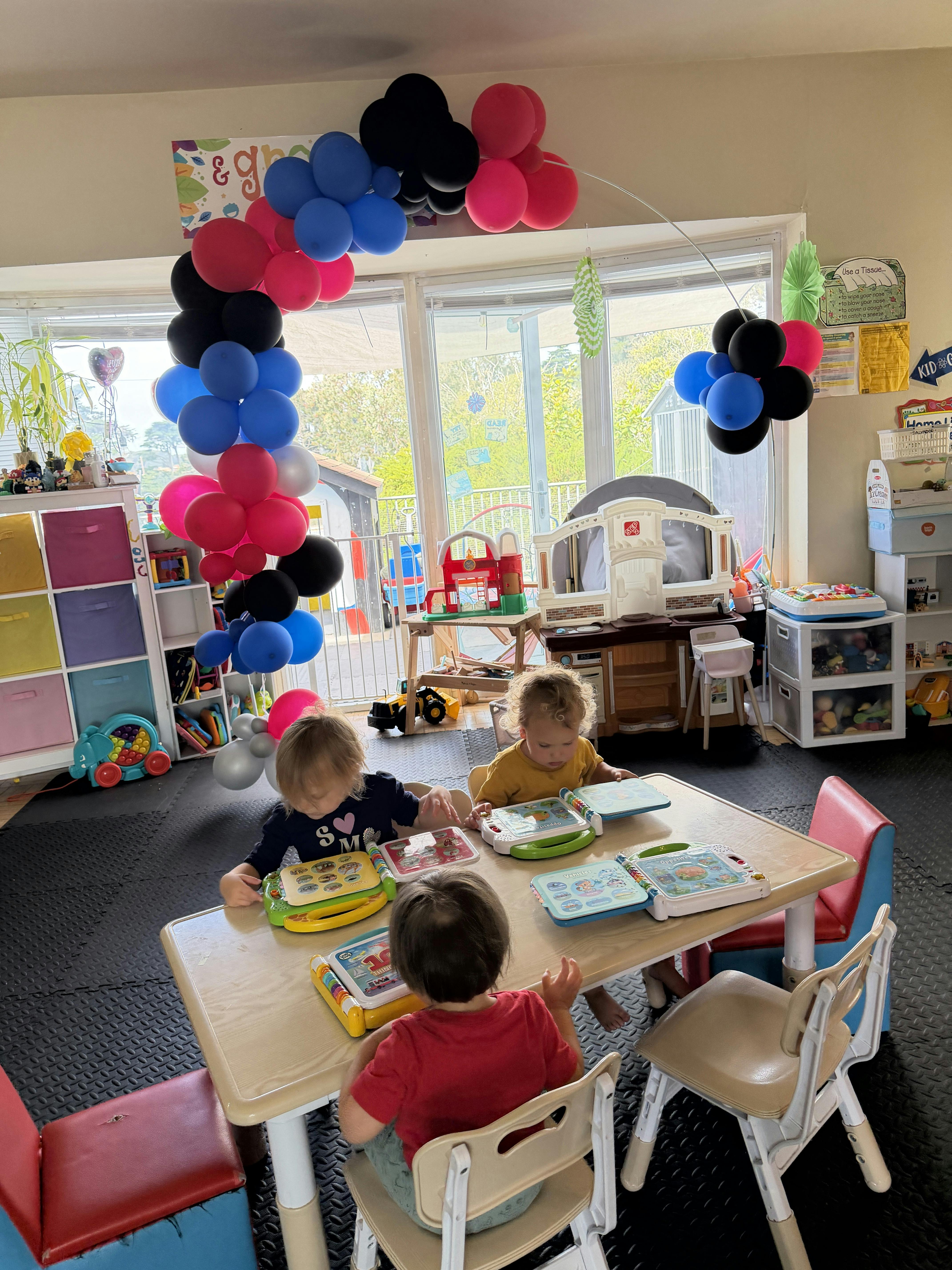 Three children sitting at a table playing with electronic books in a playroom