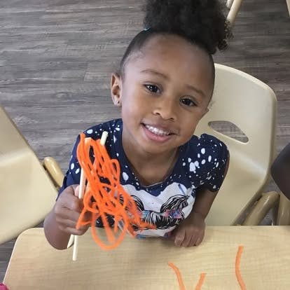 Child holding orange pipe cleaners at a table