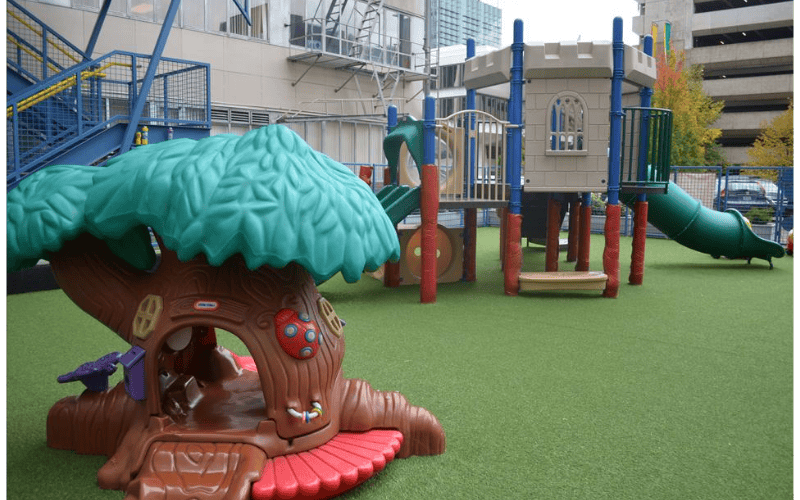 A green astroturf playground with a brown treehouse and a tan play structure