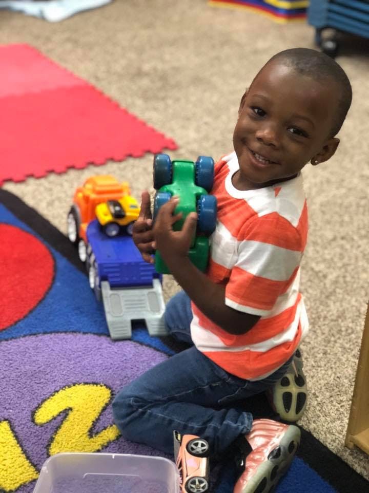 Child kneeling on a rug, holding a green toy car
