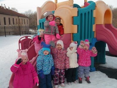 Children in winter clothing standing on and around a playground slide in snow