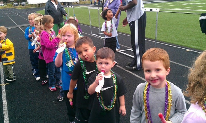 Children in a line on a track, some holding lollipops