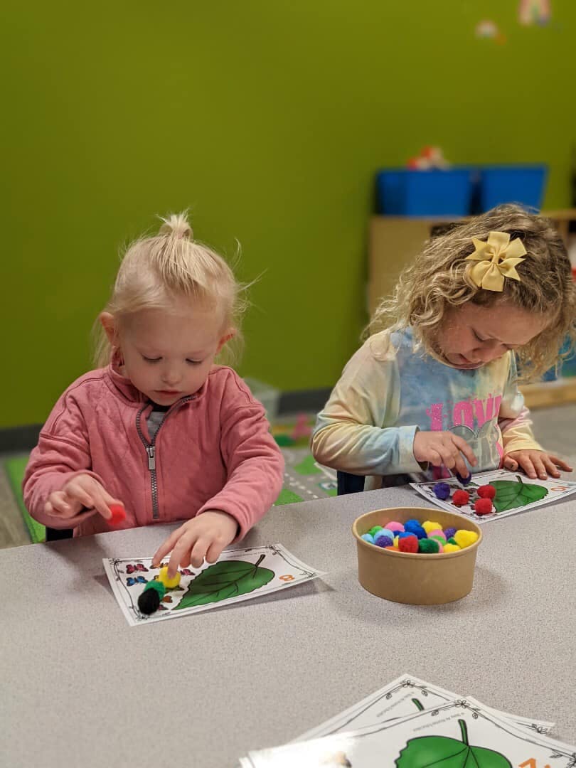 Two children doing an art activity with pom-poms and leaf cutouts