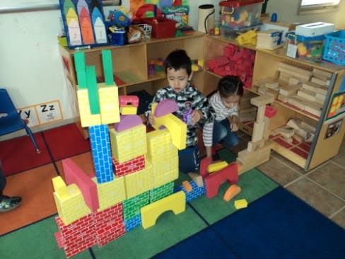 Two children playing with large colorful building blocks in a classroom