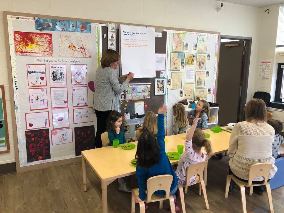 Person teaching children in a classroom, some children raising hands
