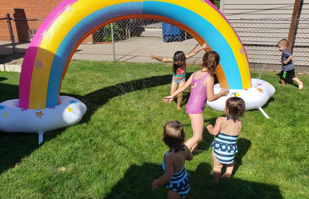 Children playing in a yard with a rainbow sprinkler