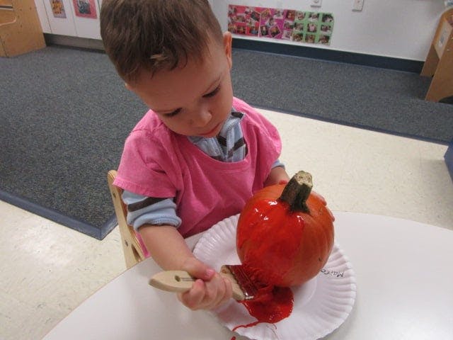 Child painting a small pumpkin red with red paint