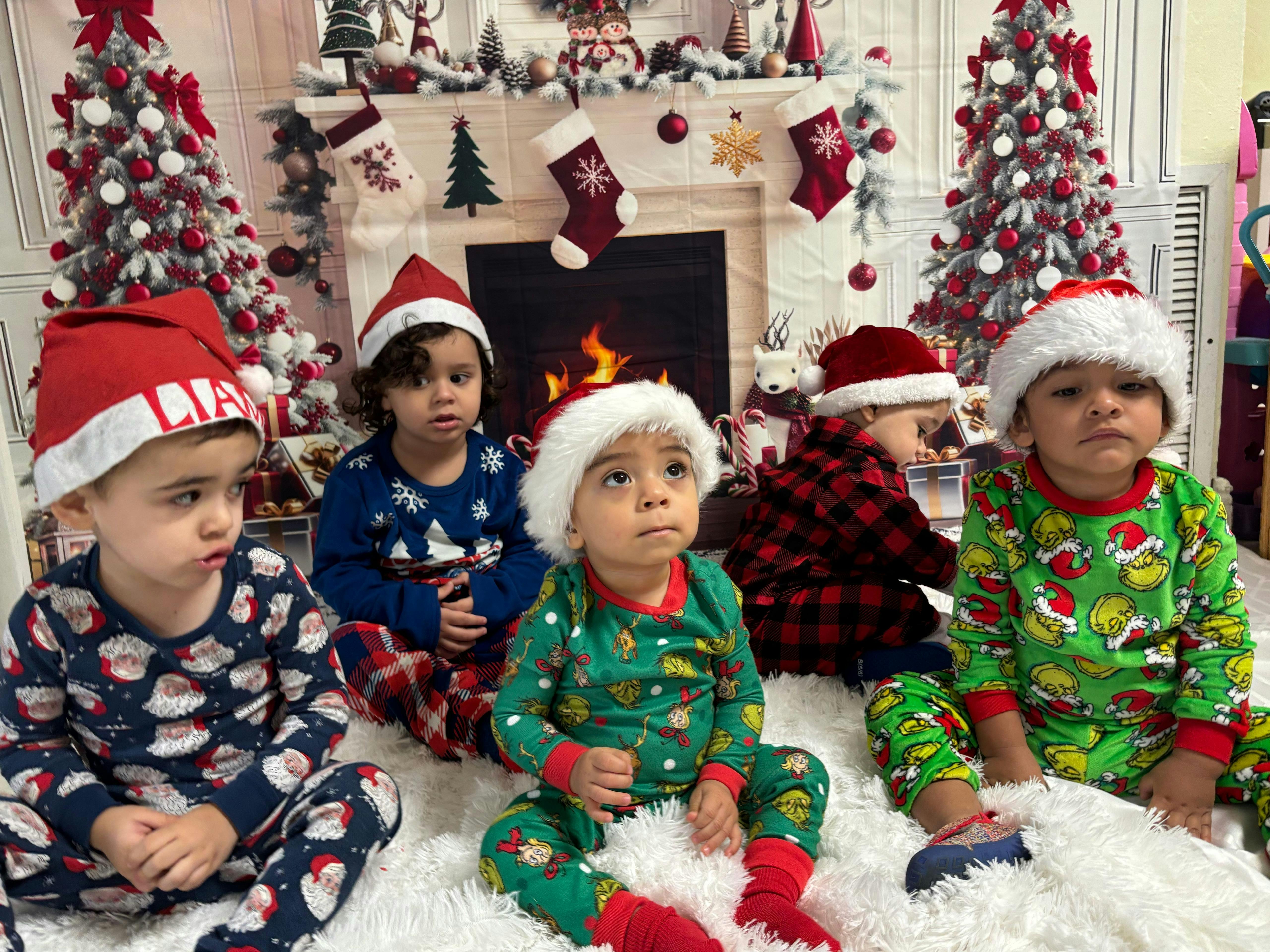 Four children in Christmas pajamas and Santa hats sitting on a white rug