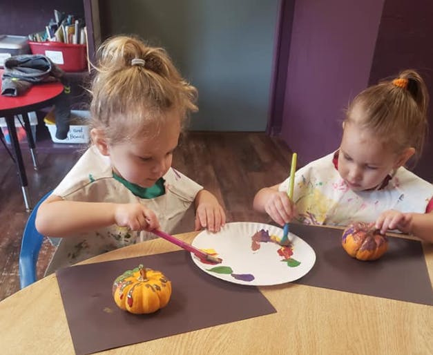 Two children painting small pumpkins at a table