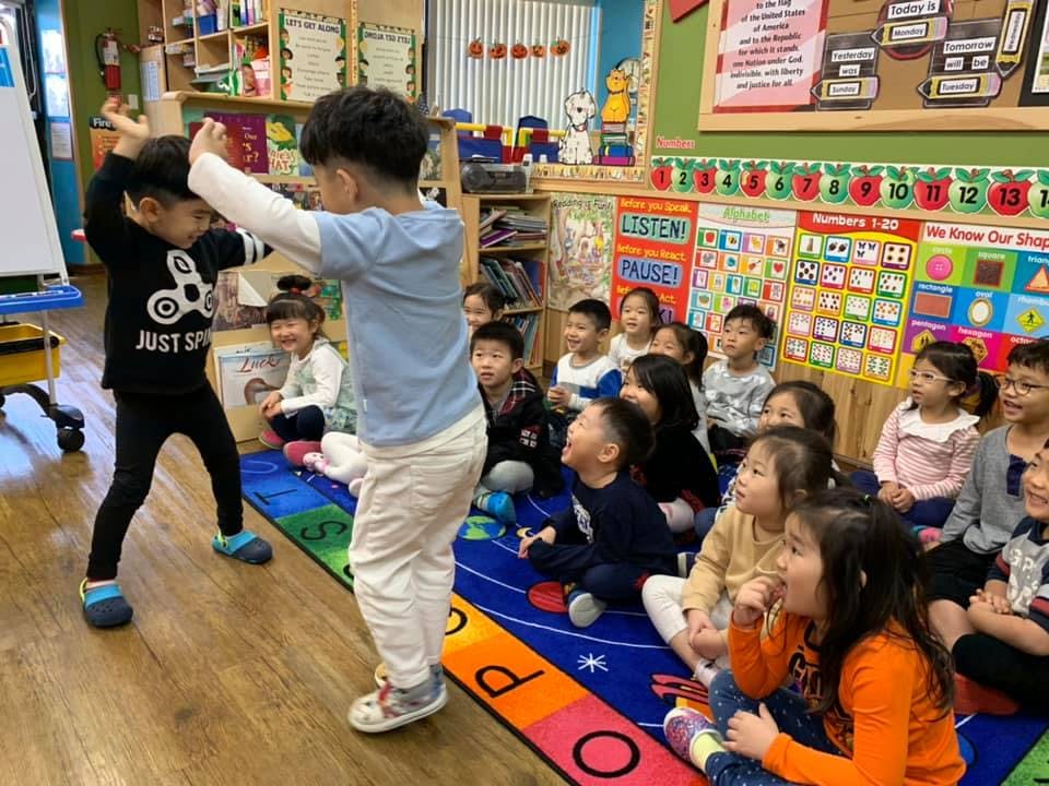 Two children playing in front of a group of children in a classroom