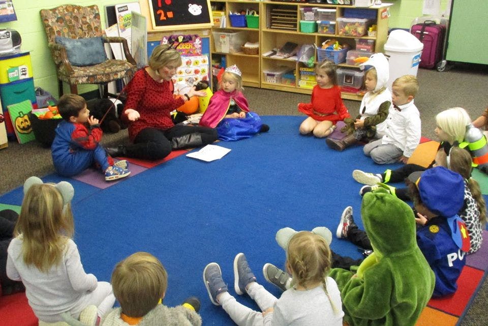 Adult and children sitting in a circle on a blue mat in a classroom