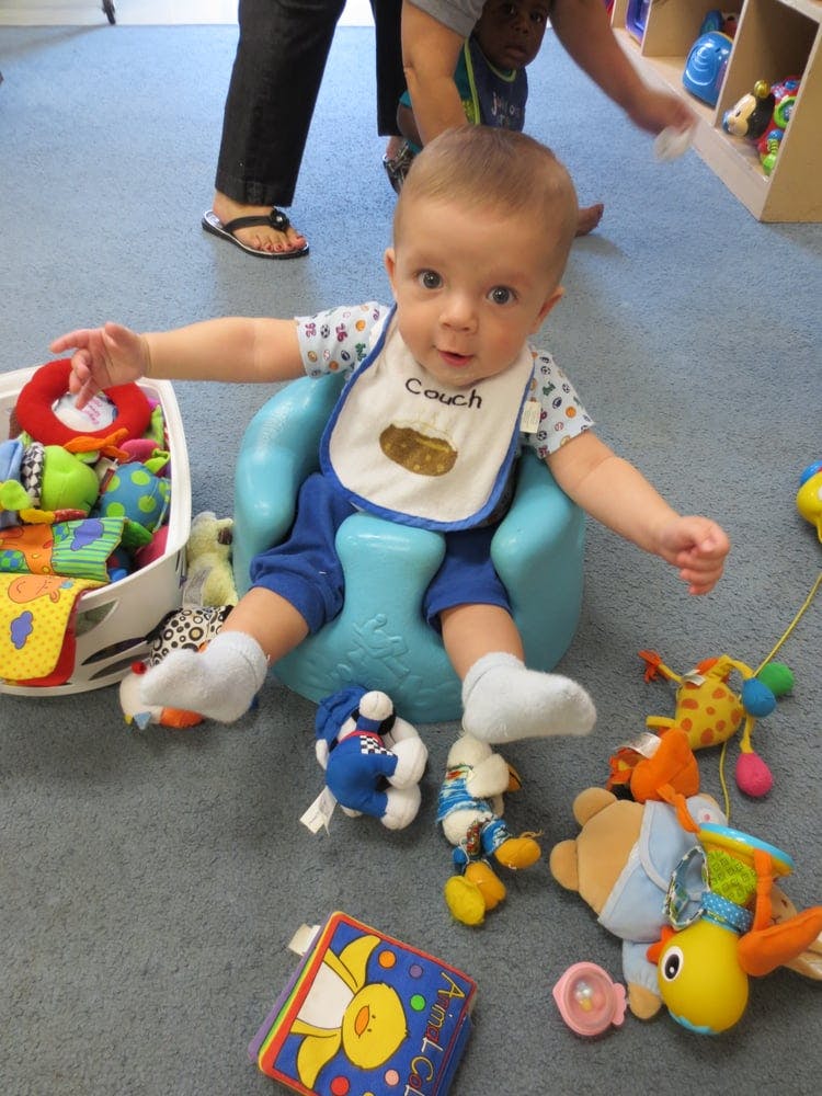 Child in a blue seat reaching for toys