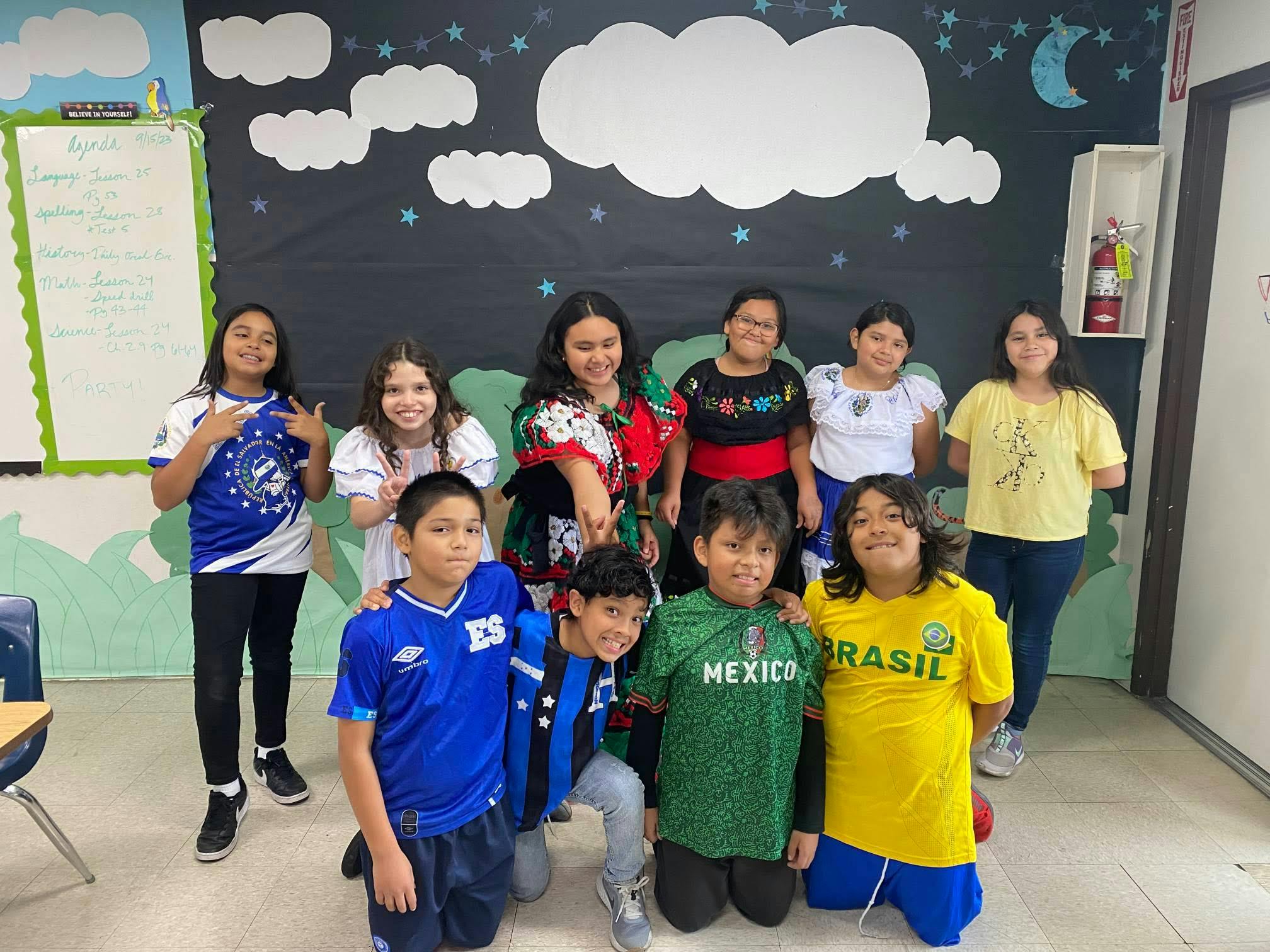 Children posing in a classroom with world flag jerseys and cultural dresses