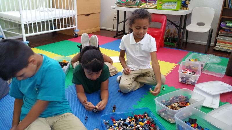 Three children playing with building blocks on a colorful mat