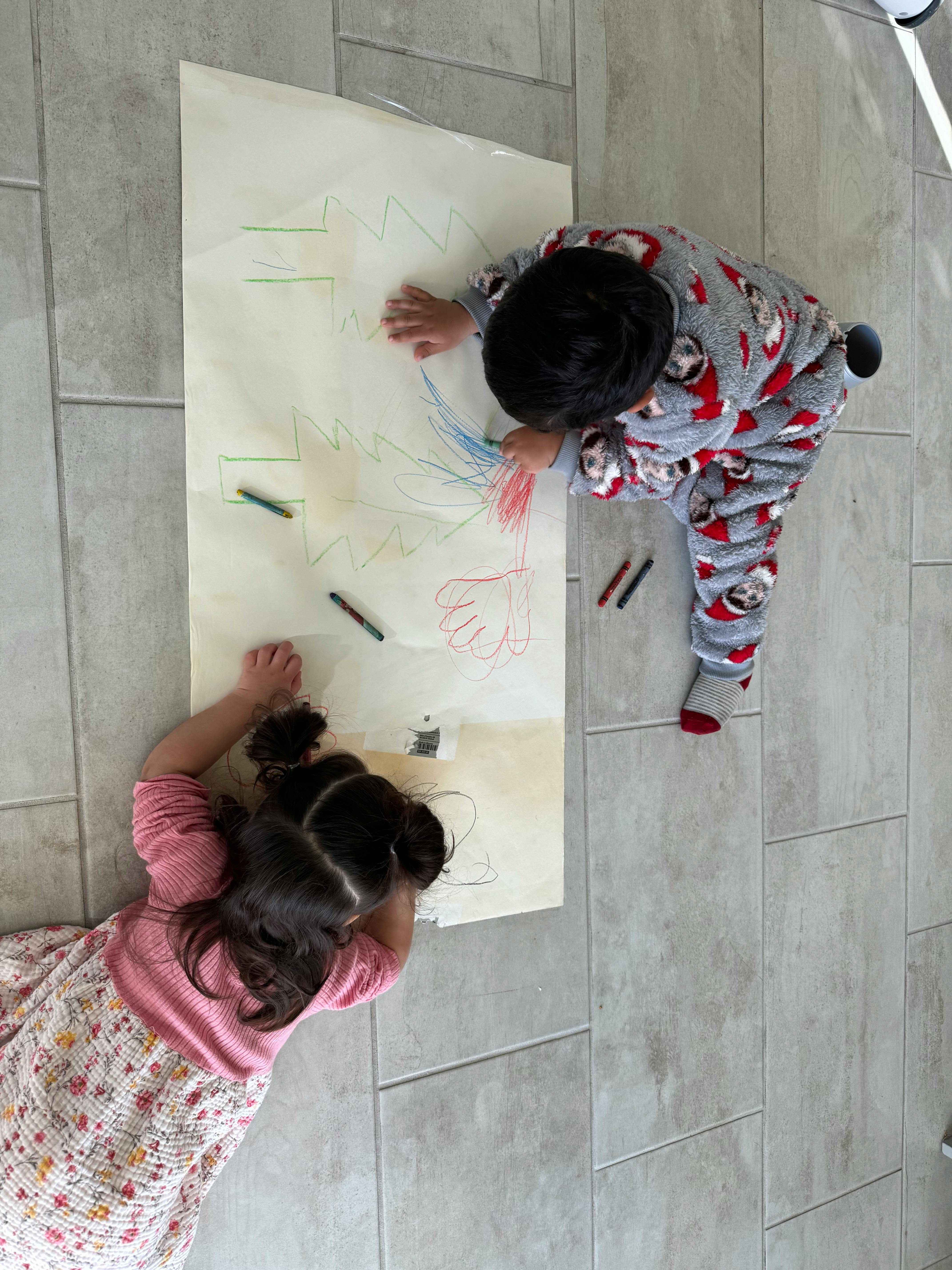 Two children drawing on a large sheet of paper on the floor