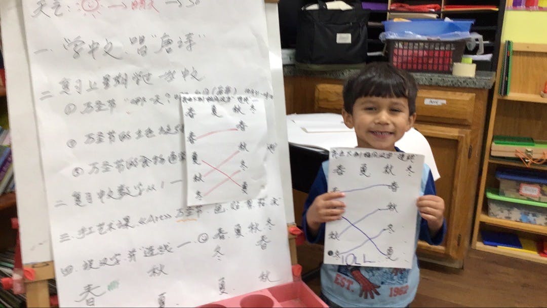 Child holding up a paper with lines drawn between characters